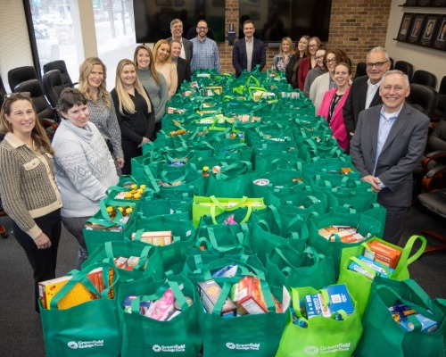 GSB staff stand around board room table covered with shopping bags filled with donated food
